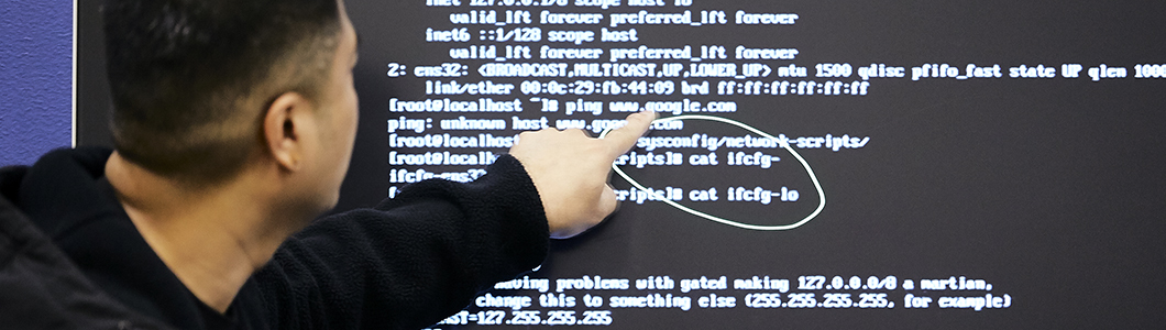 A man gestures towards a string of code displayed on a large touch screen.