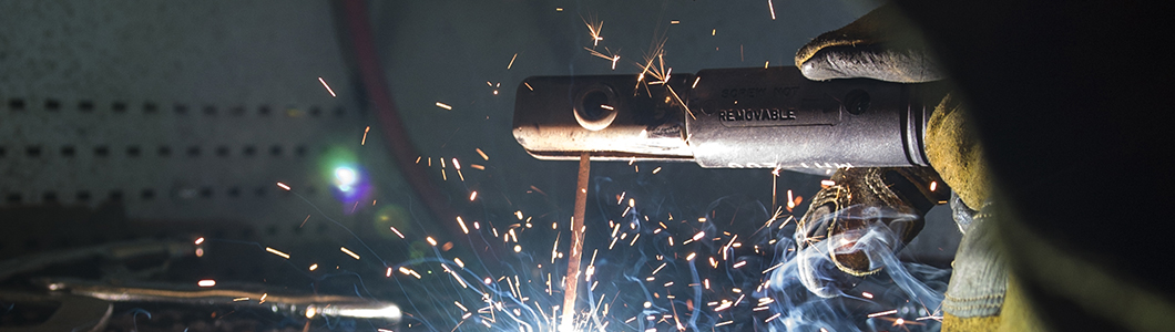 A person operates an arc welder, sparks flying.
