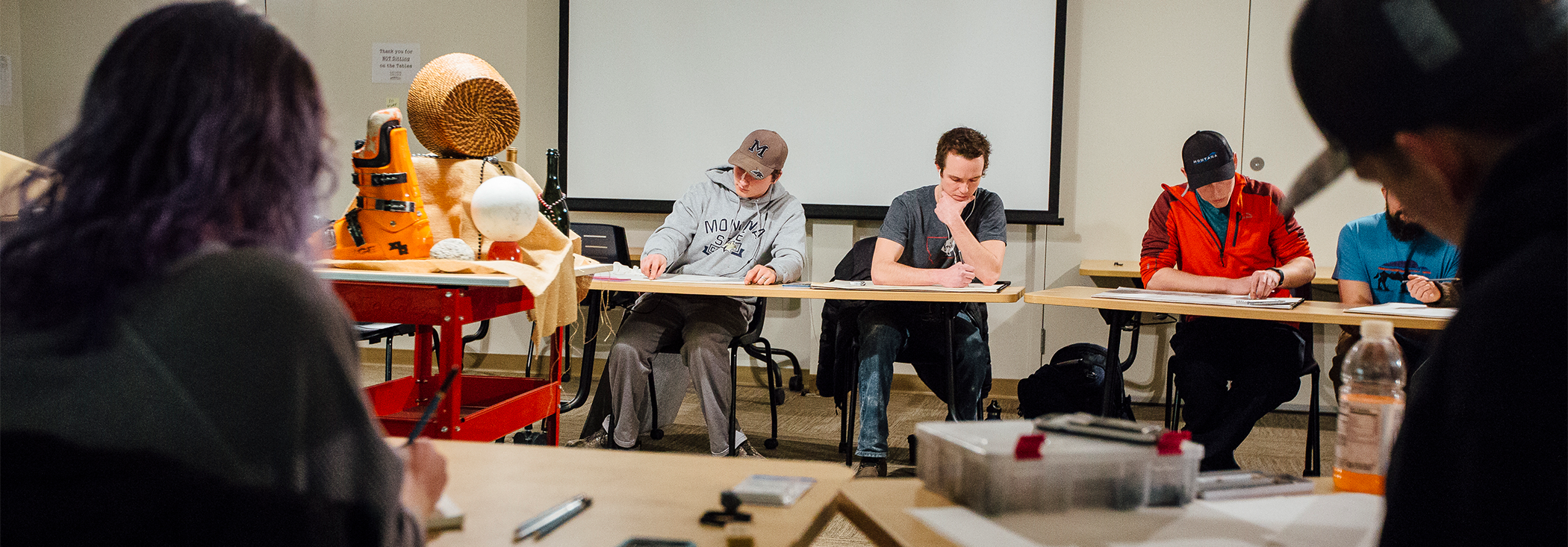 A group of students draw a still life positioned in the center of the room.